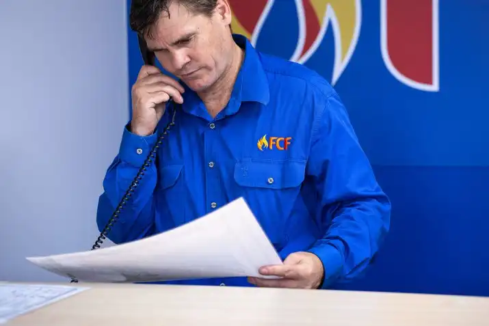 Fire safety staff reviewing documents while speaking on office phone.
