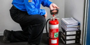 Technician inspecting fire extinguisher beside safety reports and records files.
