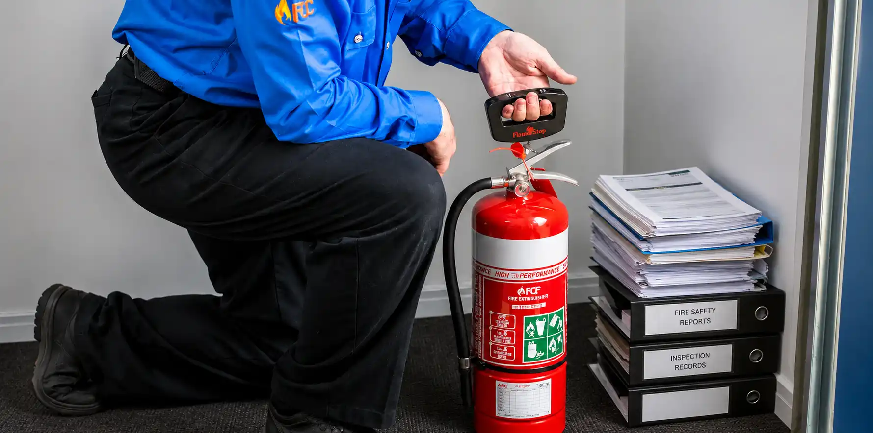 Technician inspecting fire extinguisher beside safety reports and records files.